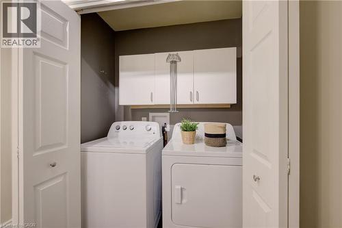 Dedicated laundry area featuring a washer and dryer, white panel bi-fold doors, white upper cabinetry, and a wood-finish shelf - 137 Wesley Crescent, Waterloo, ON 