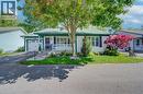White siding exterior with a dark green roof trim, featuring a covered porch with white railings, a front-facing attached garage, and a manicured lawn with mature trees and shrubbery - 137 Wesley Crescent, Waterloo, ON 
