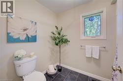 Compact bath with dark tiled flooring, a white toilet, and a single window offering exterior light - 