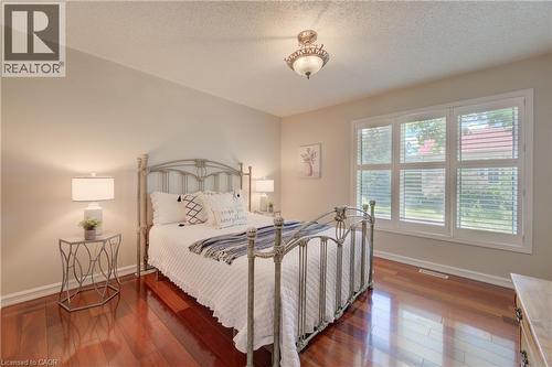 Room featuring rich wood-finish flooring, a trio of windows with plantation shutters, crown molding, and a decorative semi-flush mount ceiling fixture - 137 Wesley Crescent, Waterloo, ON 