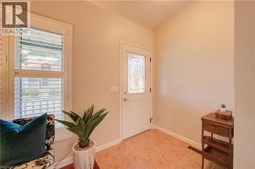 Entryway featuring terracotta-style floor tiling, a white door with decorative glass inserts, and a window with white plantation shutters - 137 Wesley Crescent, Waterloo, ON 