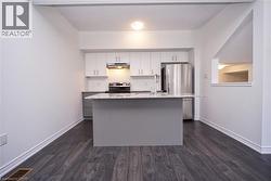 Kitchen featuring a central island with a granite-style countertop, white cabinetry with brushed nickel hardware, and stainless steel appliances - 