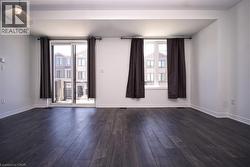 Spacious interior featuring dark wood-finish flooring, white walls, and bright natural light from multiple windows and a sliding glass door - 