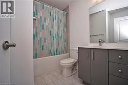 Bathroom featuring a white tub, toilet, and a vanity with gray cabinetry and a light-toned countertop - 