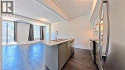 Open-concept living area with dark wood-finish flooring, a kitchen island featuring a double sink and light-colored granite countertop, and stainless steel appliances - 