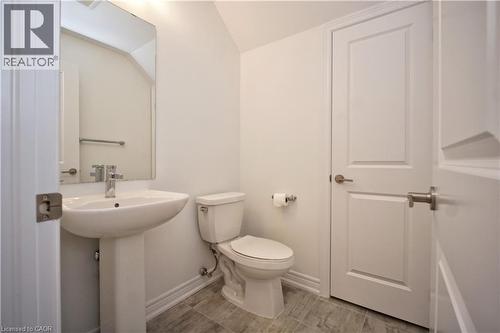 Pedestal sink with chrome faucet, large rectangular mirror, and light gray wood-finish floor tiling - 10 Birmingham Drive Unit# 129, Cambridge, ON - Indoor Photo Showing Bathroom