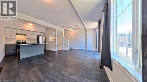 Open-concept living space featuring wood-finish flooring, a modern kitchen island with seating, stainless steel appliances, and a staircase with a dark wood handrail - 10 Birmingham Drive Unit# 129, Cambridge, ON - Indoor Photo Showing Kitchen