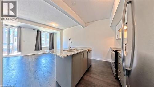 Open-concept living area with dark wood-finish flooring, a kitchen island featuring a double sink and light-colored granite countertop, and stainless steel appliances - 10 Birmingham Drive Unit# 129, Cambridge, ON - Indoor Photo Showing Kitchen With Stainless Steel Kitchen With Double Sink