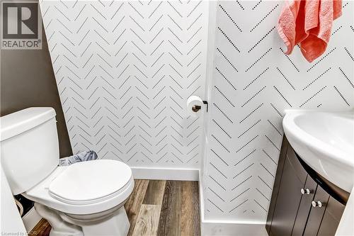 Powder room featuring contemporary patterned wallpaper, a white toilet, and a dark wood-finish vanity with a semi-recessed sink - 218 Richardson Drive Unit# 26, Port Dover, ON 