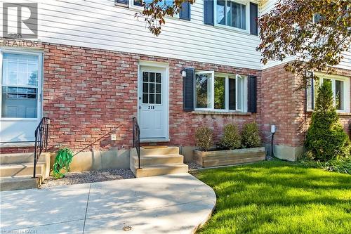 Brick and siding exterior featuring multiple entry doors, a curved concrete walkway, and established landscaping with a wooden planter box - 218 Richardson Drive Unit# 26, Port Dover, ON 