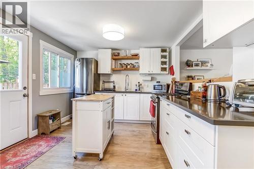 Bright kitchen featuring white cabinetry, dark countertops, a stainless steel refrigerator, a movable island with a light-toned top, and wood-finish flooring - 218 Richardson Drive Unit# 26, Port Dover, ON 