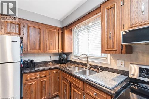 Kitchen featuring wood cabinetry, dark-toned countertops, a stainless steel double-basin sink with a gooseneck faucet, and a tiled backsplash - 366 Berkindale Drive, Hamilton, ON 