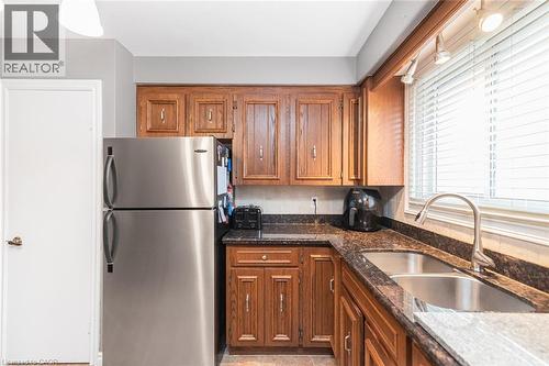 Kitchen featuring wood cabinetry, dark granite-look countertops, and a stainless steel double-basin sink with a gooseneck faucet - 366 Berkindale Drive, Hamilton, ON 