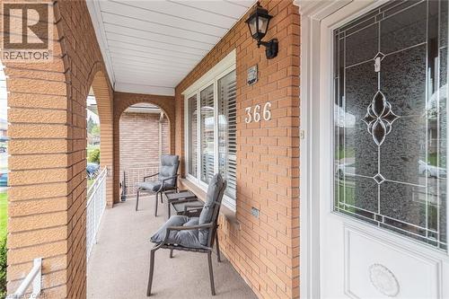 Covered front porch featuring arched brickwork, a decorative glass entry door, white window blinds, an exterior wall sconce, and a white metal railing - 366 Berkindale Drive, Hamilton, ON 