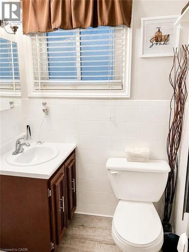 Bathroom featuring a window with white blinds, white wall tiling, a white toilet, and wood-finish flooring - 366 Berkindale Drive, Hamilton, ON 