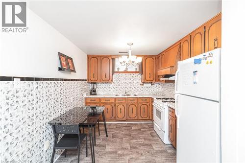 Kitchen featuring wood cabinetry, white appliances, patterned backsplash, and wood-finish flooring - 366 Berkindale Drive, Hamilton, ON 