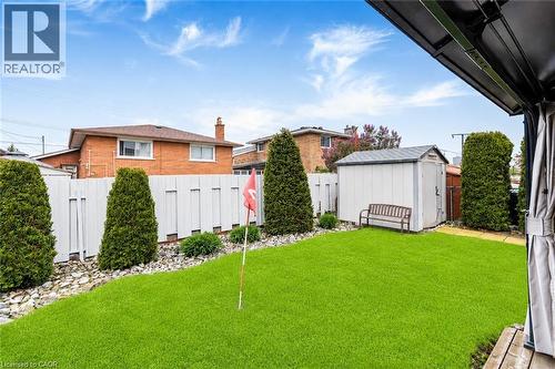Spacious backyard featuring an artificial turf lawn, privacy fencing, mature evergreen shrubs, and a storage shed - 366 Berkindale Drive, Hamilton, ON 