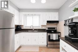 Kitchen featuring white cabinetry, dark speckled countertops, stainless steel appliances, a tile backsplash, and a window with blinds - 