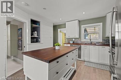 Kitchen featuring a central island with a wood-finish countertop, white cabinetry with dark hardware, wood-finish flooring, and a subway tile backsplash - 33 Huxley Avenue N, Hamilton, ON 