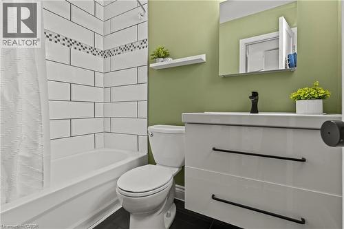 Bathroom featuring a white subway tile shower surround with a decorative accent band, a white bathtub, and dark flooring - 33 Huxley Avenue N, Hamilton, ON 