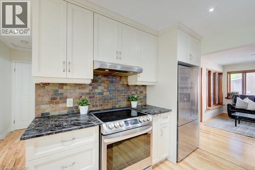 Kitchen featuring light-toned cabinetry, multi-toned tile backsplash, dark stone countertops, and stainless steel appliances - 60 Mayfield Avenue, Waterloo, ON 