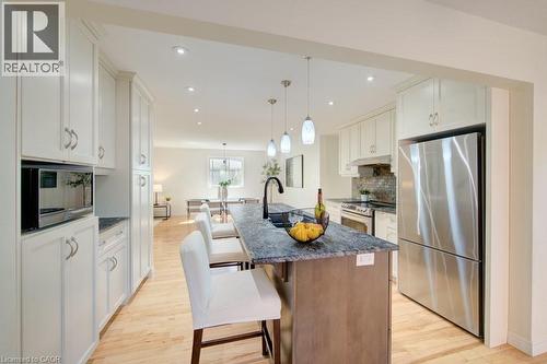 Modern kitchen featuring a central island with a dark countertop and pendant lighting, stainless steel appliances, extensive white cabinetry, and wood-finish flooring - 60 Mayfield Avenue, Waterloo, ON 