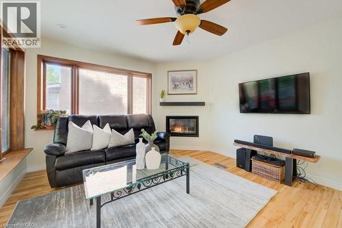 Living area featuring a corner fireplace with a dark mantel, wood-finish flooring, and a ceiling fan with light fixture - 60 Mayfield Avenue, Waterloo, ON 