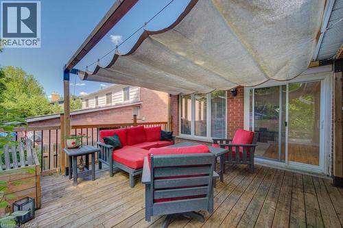 Expansive wood-finish deck featuring a retractable fabric awning, full-height sliding glass doors, brick exterior, and wood railing - 60 Mayfield Avenue, Waterloo, ON 