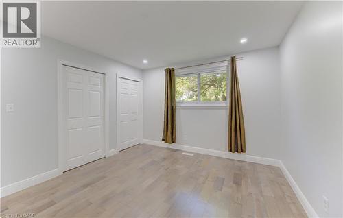 Room featuring wood-finish flooring, two white bi-fold doors, a large window with white trim, and recessed ceiling lighting - 80 Lower Canada Crescent, Kitchener, ON 