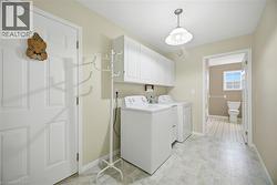 Functional laundry area featuring upper white cabinetry, a light-toned flooring, and a ceiling-mounted light fixture - 
