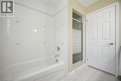 Bathroom featuring a white subway tile surround with decorative accents, a white soaking tub, and a separate shower with a frosted glass door - 