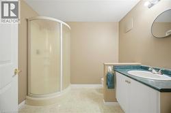 Bathroom featuring a curved shower enclosure, a vanity with an integrated sink, a dark green countertop, a white vanity cabinet with silver-toned hardware, and light-toned flooring - 