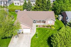Brick exterior featuring a covered front porch with white railing, attached two-car garage, concrete driveway, and established front yard landscaping - 