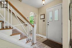 Entryway featuring a staircase with carpeted treads and a wood handrail, ceramic tile flooring, and a door with decorative glass inserts - 
