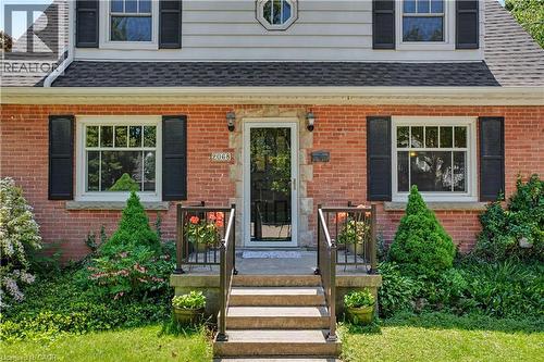 Brick facade residence featuring a front entry porch with stone steps, dark metal railings, and dual exterior wall lanterns - 2068 Wellington Avenue, Burlington, ON 