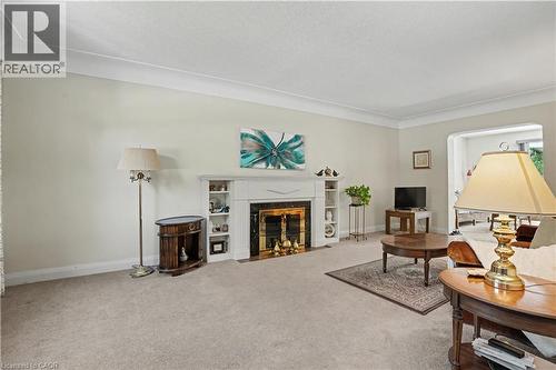 Living room featuring a fireplace with a white mantel, built-in shelving, light-toned carpeting, and crown molding - 2068 Wellington Avenue, Burlington, ON 