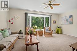 Living area featuring a spacious bay window, ceiling fan, and neutral carpet flooring - 