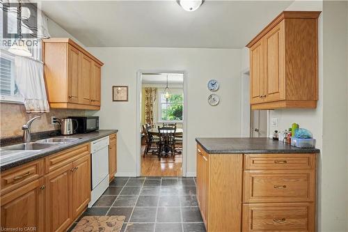 Kitchen featuring abundant wood cabinetry, dark countertop surfaces, a double basin stainless steel sink, and durable tile flooring - 2068 Wellington Avenue, Burlington, ON 