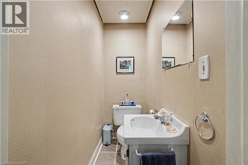 Compact powder room featuring a wall-mounted sink with chrome faucet, a toilet, and textured beige wallpaper - 2068 Wellington Avenue, Burlington, ON 