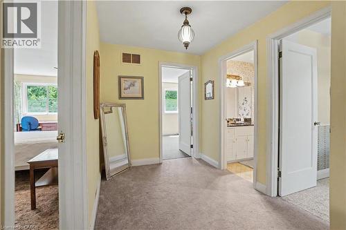 Carpeted hallway with a hanging light fixture and access to three separate rooms - 2068 Wellington Avenue, Burlington, ON 