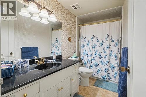 Bathroom featuring a vanity with a dark countertop and black undermount sink, brass-finish faucet, and white louvered cabinetry - 2068 Wellington Avenue, Burlington, ON 
