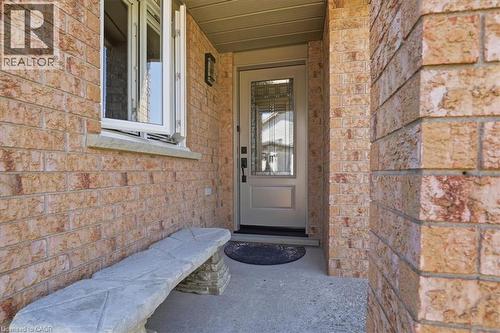 Front entry featuring a light-colored door with decorative glass inserts, brick exterior, concrete porch, and an exterior wall sconce - 20 Ridgeway Crescent, Kitchener, ON - Outdoor With Exterior