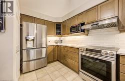 Contemporary kitchen featuring stainless steel appliances, light wood-finish cabinetry, a white subway tile backsplash, and light-toned tile flooring - 