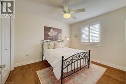 Room featuring wood-finish flooring, a ceiling fan with integrated lighting, a window with plantation shutters, and a bi-fold closet door - 