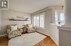 Hardwood-finish flooring featuring a plush area rug, a built-in wall shelf, and a large window with white plantation shutters - 