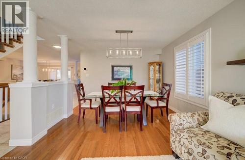Dining area featuring wood-finish flooring, a contemporary linear chandelier, and a window with white plantation shutters - 7 Housler Lane, Cambridge, ON 