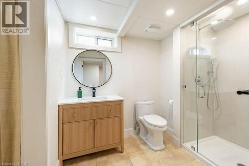 Contemporary bathroom featuring a wood-finish vanity with a white countertop and round mirror - 22 Charlotte Crescent, Kitchener, ON 