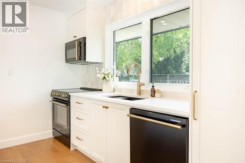 Kitchen featuring white cabinetry with brass hardware, a black appliance suite, white countertops, and a large window above the sink - 22 Charlotte Crescent, Kitchener, ON 