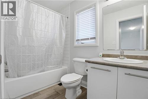 Bathroom featuring a white tub with subway tile surround, wood-finish flooring, and a window with horizontal blinds - 7 Upper Mercer Street Unit# G30, Kitchener, ON - Indoor Photo Showing Bathroom