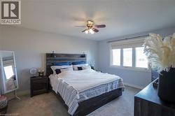 Carpeted bedroom featuring light blue walls, a contemporary ceiling fan, and a triple window with roller shades - 